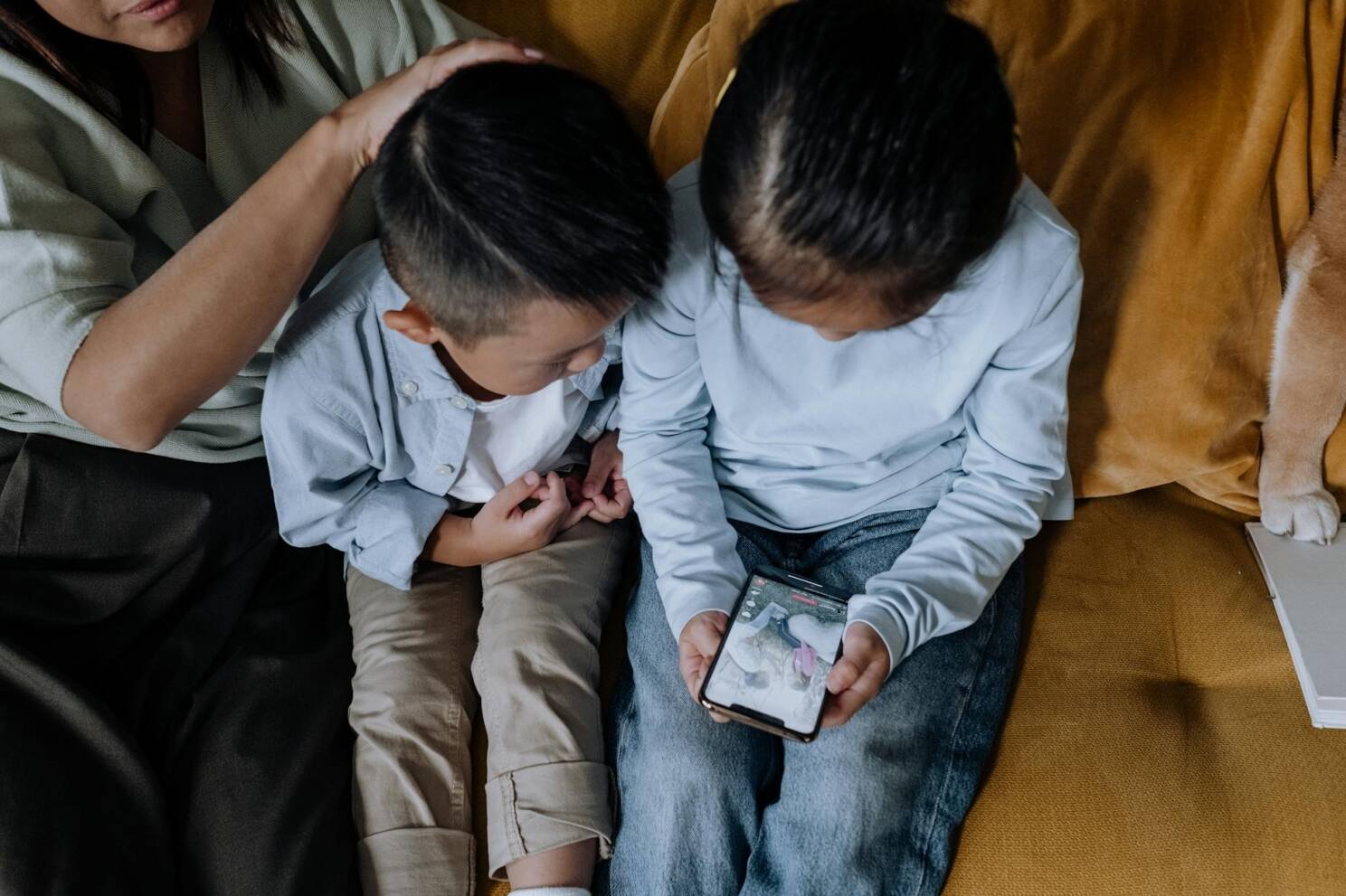 Two kids sharing a smartphone while sitting with family on a cozy couch.