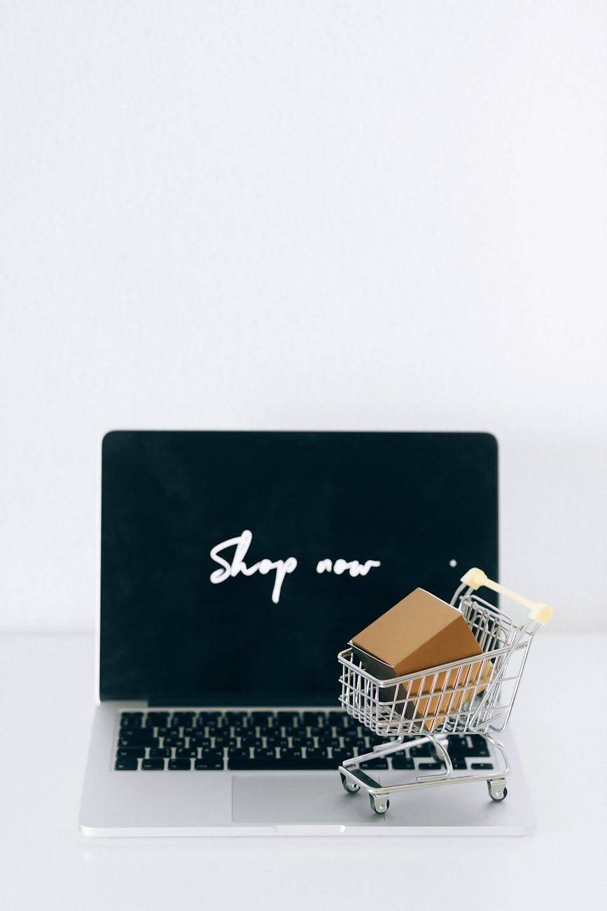 A laptop screen displaying 'Shop now' with a miniature shopping cart and cardboard box.