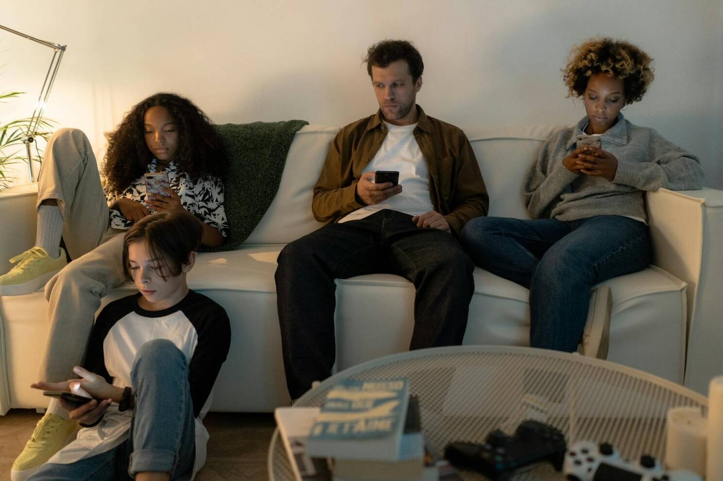 A diverse family sits on a sofa using their smartphones together indoors.