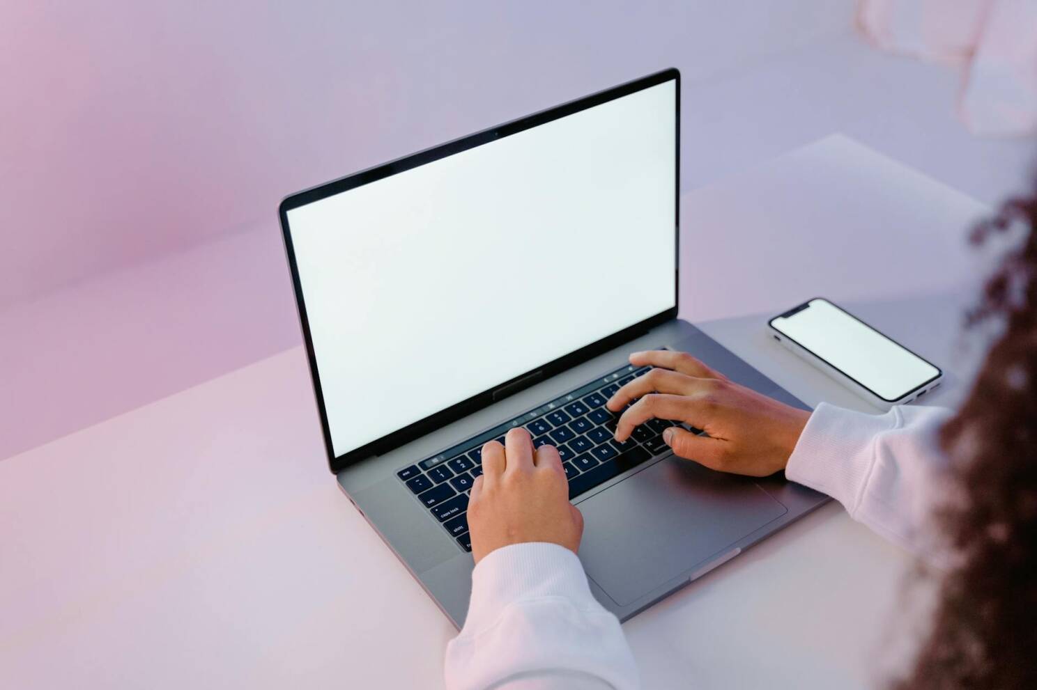 A person working on a laptop with a blank screen and smartphone on a desk.